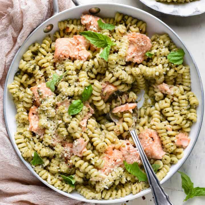 Overhead photo of skillet filled with spiral shaped noodles tossed with pesto, and chunks of salmon.
