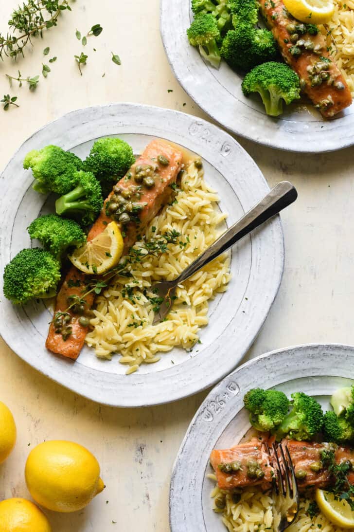 Fish with lemon caper sauce, served on a rustic plate with orzo and steamed broccoli.
