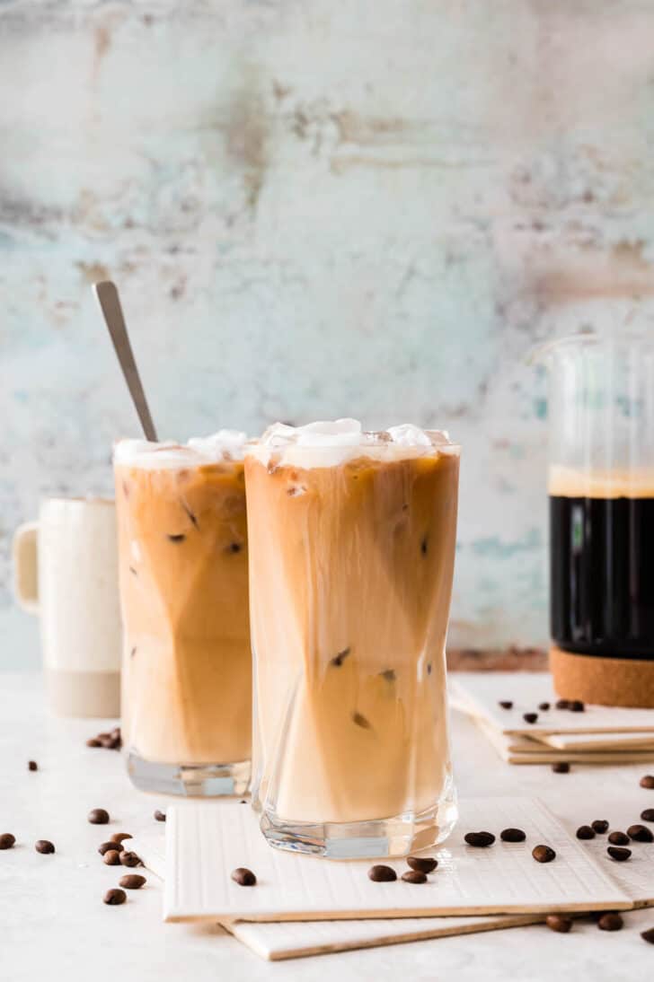 Two large glasses of salted caramel cream cold brew coffee, with coffee beans garnishing the scene.