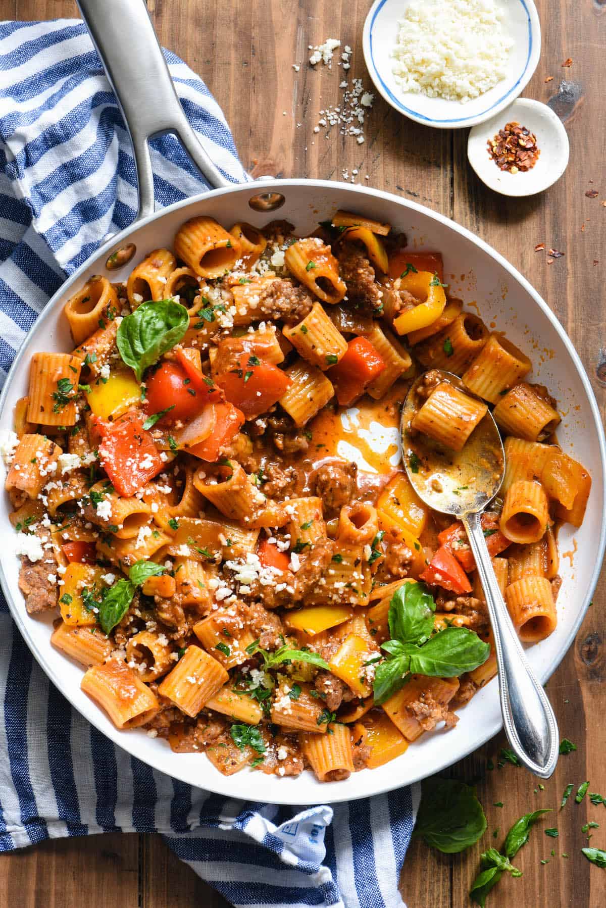 A white skillet filled with an Italian sausage pasta recipe topped with fresh herbs.