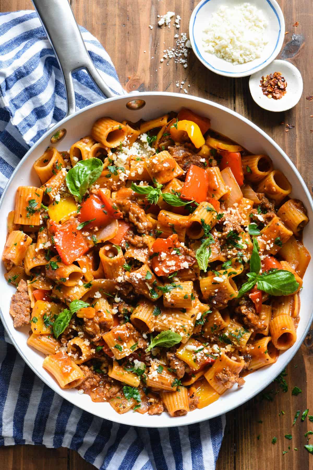 A white skillet filled with pasta with sausage and peppers topped with fresh herbs.