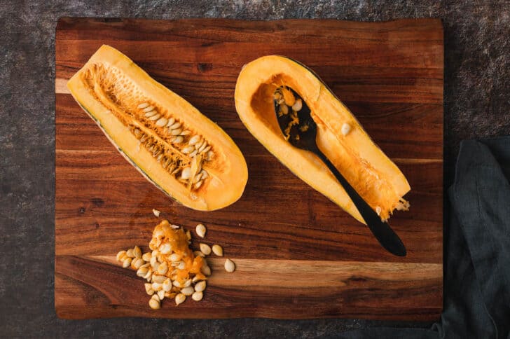 A photo demonstrating how to prepare delicata squash by using a spoon to scoop out the seeds.