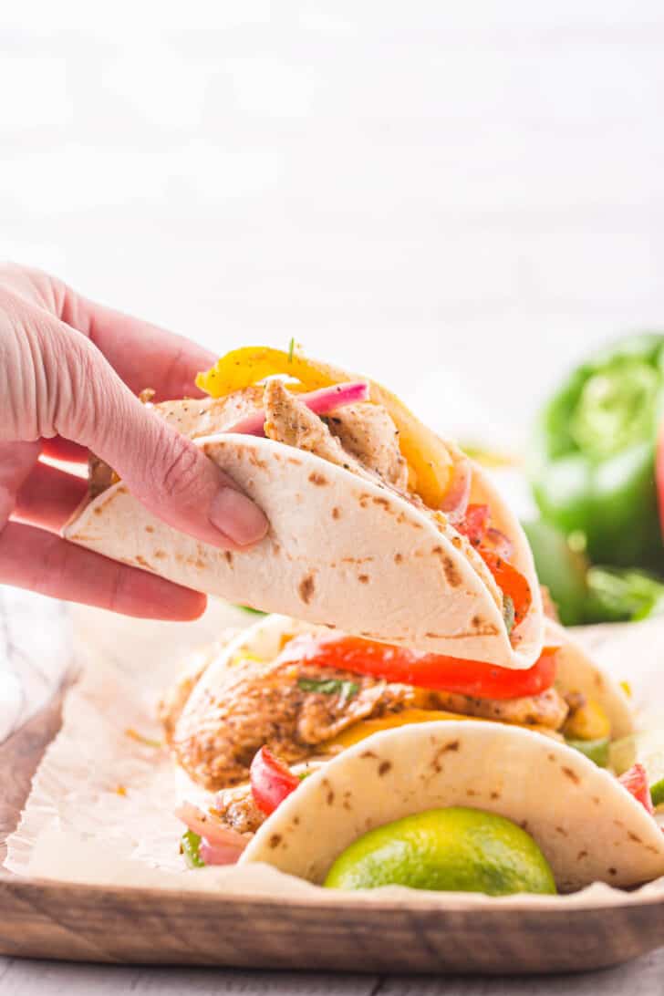 A hand holding up a flour tortilla filled with easy sheet pan chicken fajitas.
