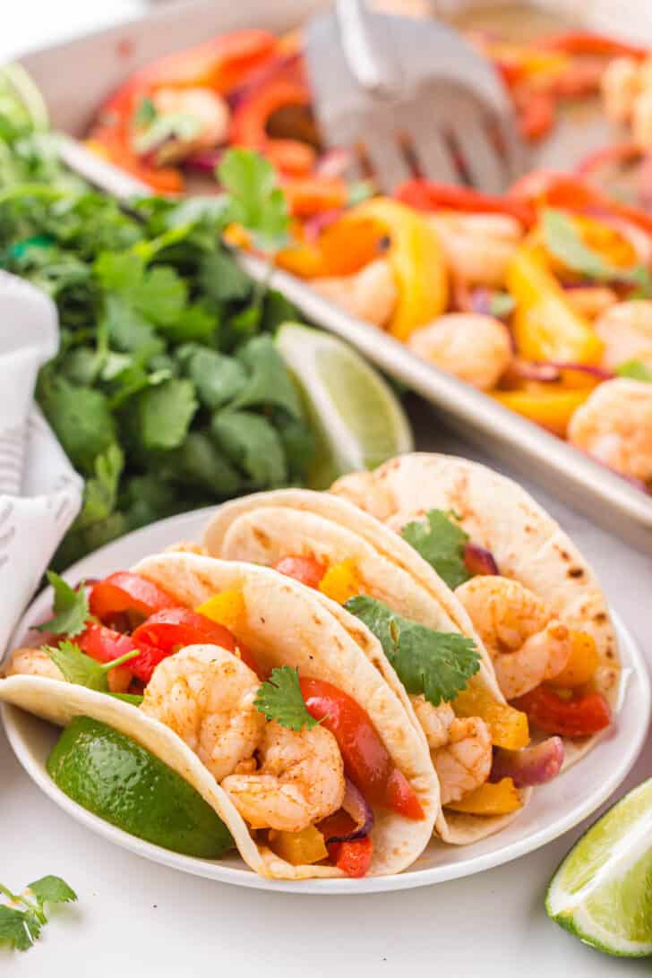 Flour tortillas filled with roasted shrimp and bell peppers, with cilantro and a sheet pan in the background.