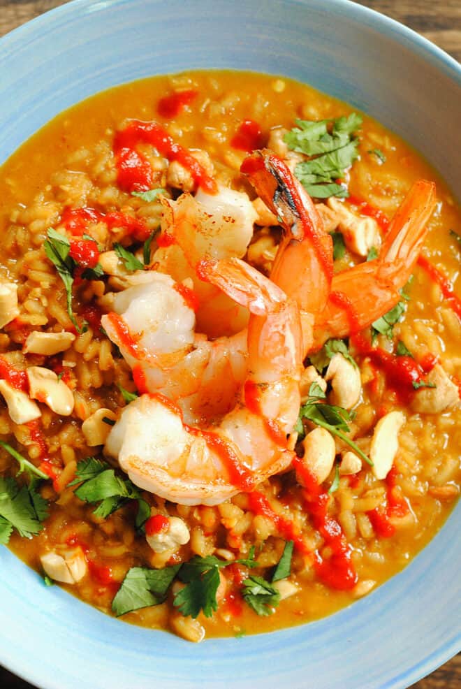 Three large shrimp on top of spicy orange rice dish, garnished with cilantro.