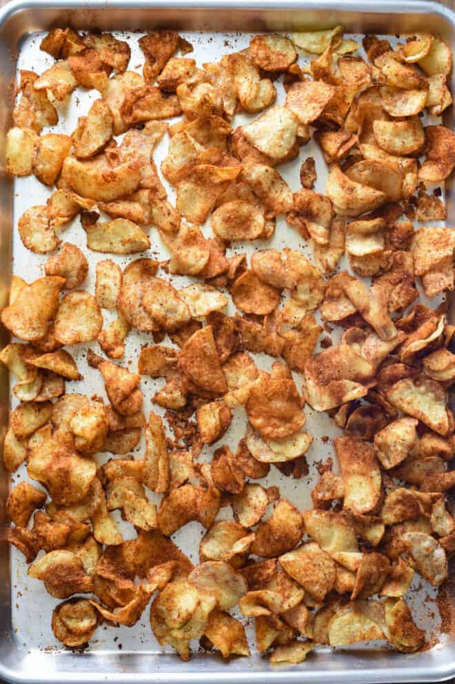Stainless steel sheet pan of hot potato chips covered in spices.