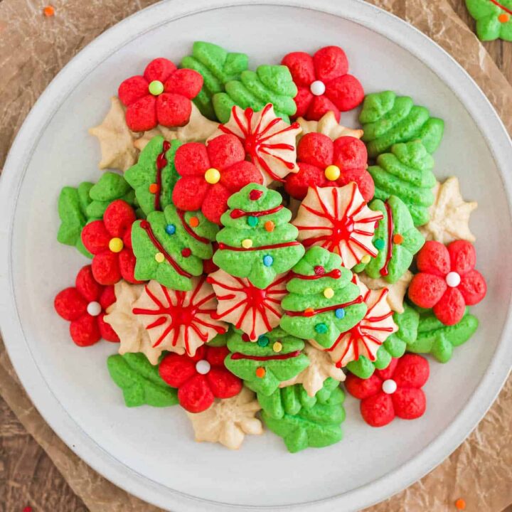 A white plate topped with red, green and white spritz cookies decorated with icing and sprinkles.