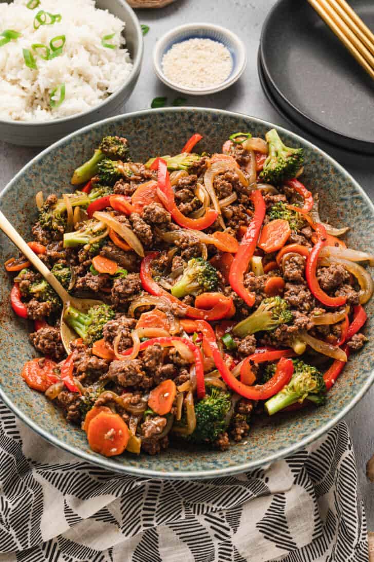 A textured light blue bowl filled with ground beef stir fry and veggies.