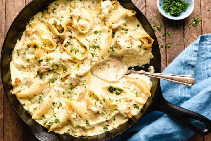 A cast iron skillet filled with stuffed alfredo shells, with a spoon scooping some sauce out.