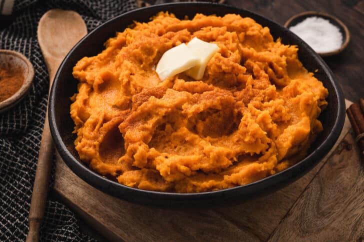 Mashed instant pot sweet potatoes topped with pats of butter in a black bowl.