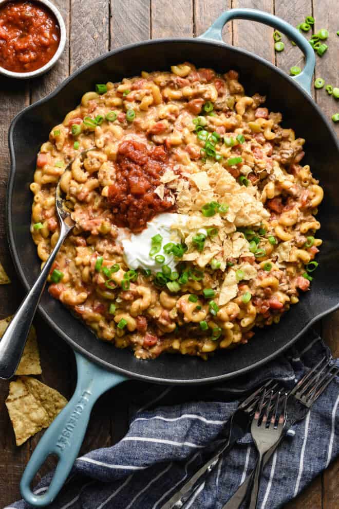 Large skillet filled with taco mac and cheese, toped with salsa, sour cream crushed tortilla chips and green onions.