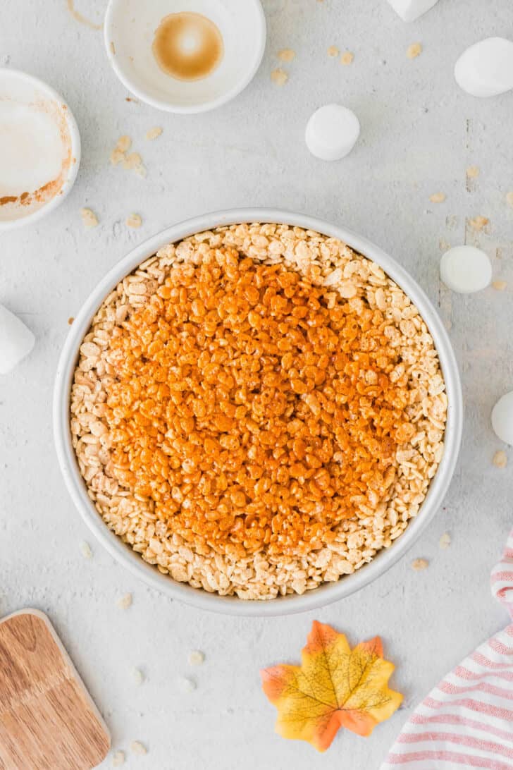 A round cake pan filled with cereal dessert, the center of which has been dyed orange to resemble a pumpkin pie.