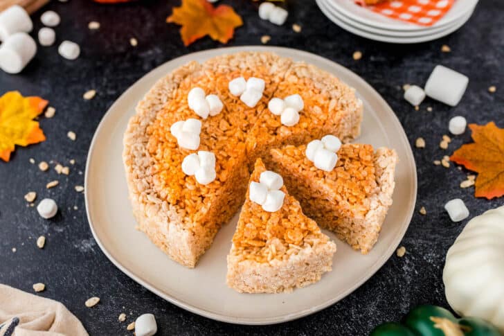 Thanksgiving Rice Krispies treats, shaped and cut into pie "slices," topped with marshmallows, on a round white plate.