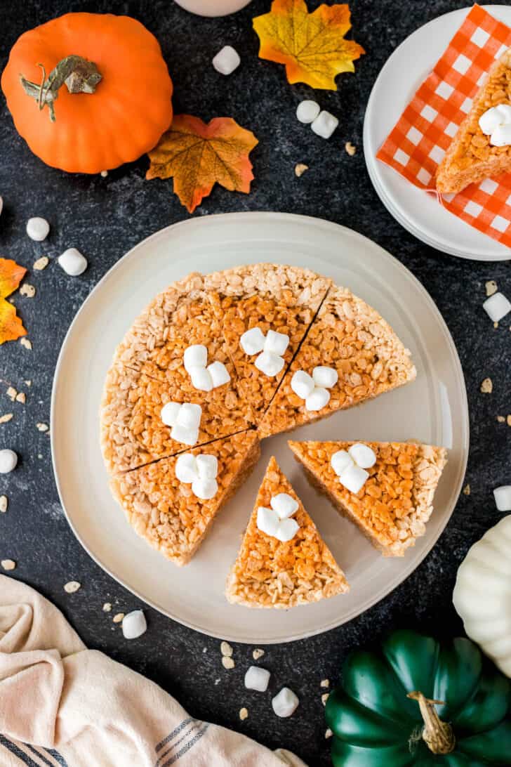 Thanksgiving Rice Krispies treats colored and shaped to resemble a pumpkin pie, on a white plate on a dark surface.
