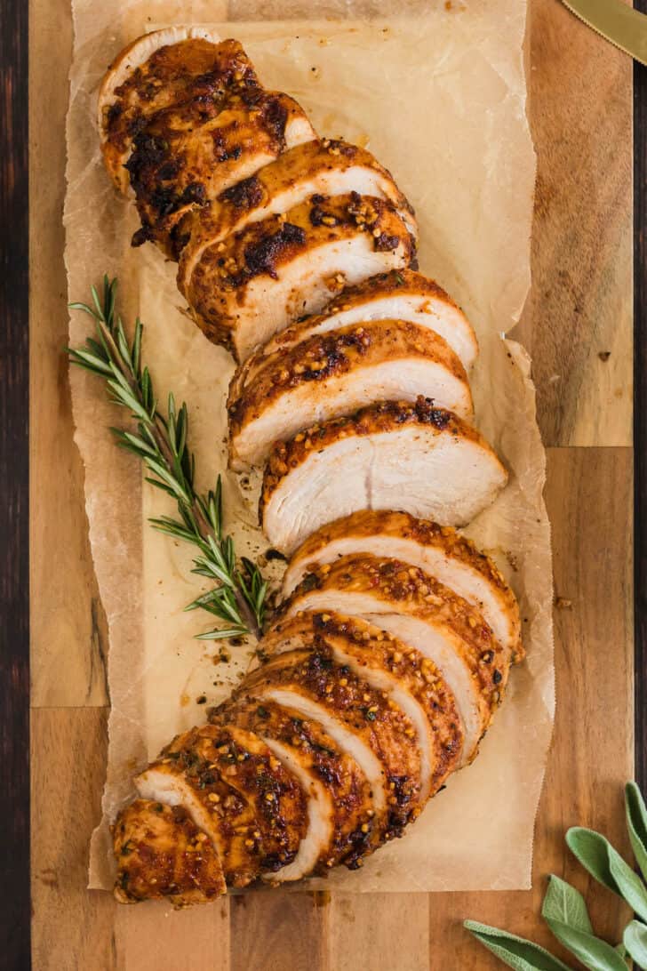 Sliced turkey breast tenderloin on a wooden cutting board, garnished with rosemary.