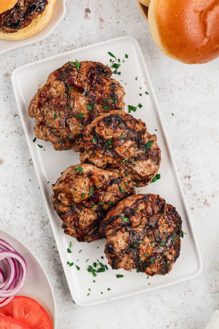 Cooked turkey burgers on a white plate sprinkled with parsley.