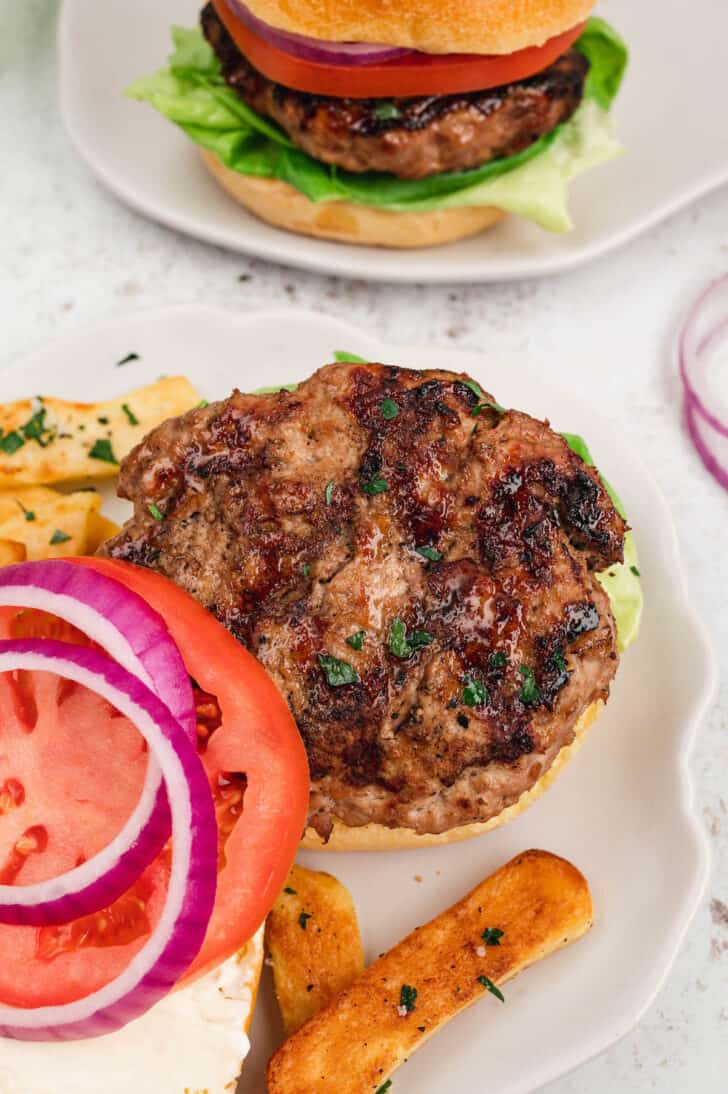 An open face turkey burger on a plate alongside red onion and tomato.