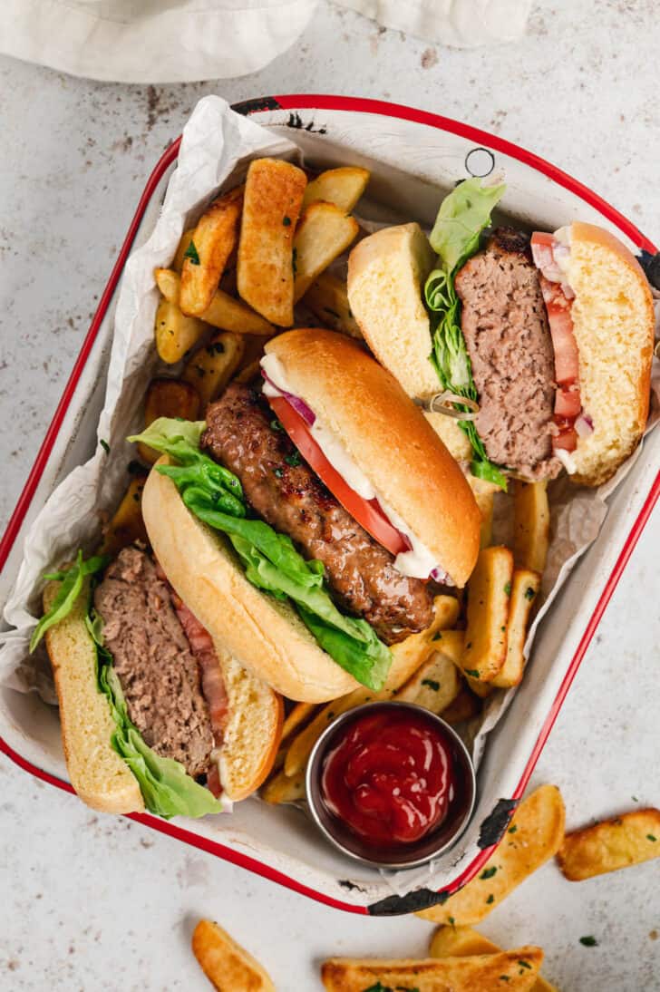 Whole and halved turkey burgers arranged on their sides in a red and white baking pan on top of thick cut fries.
