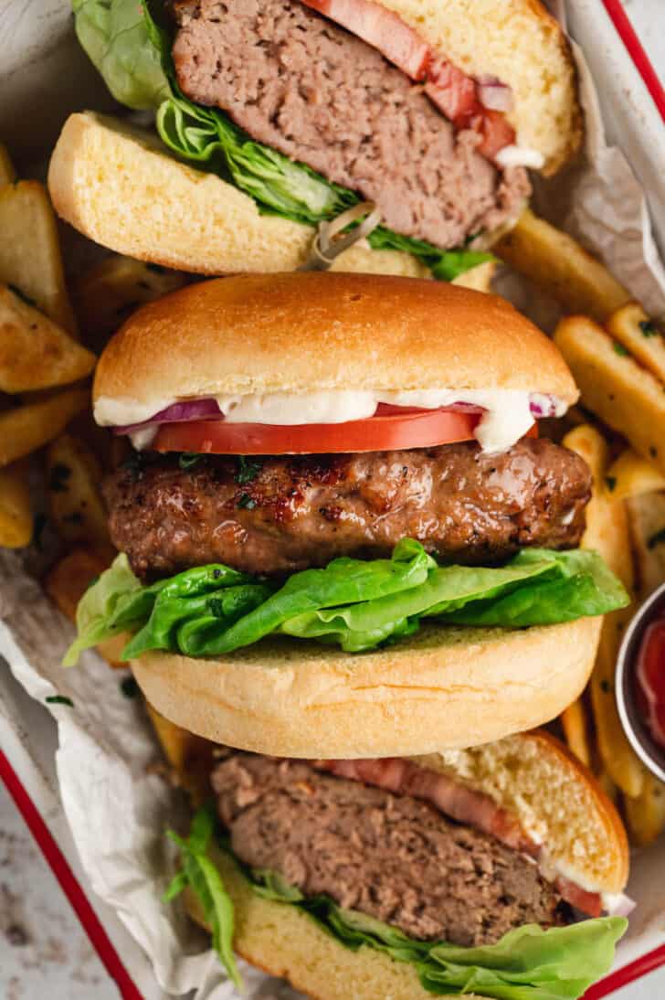 Whole and halved turkey burgers arranged on their sides in a red and white baking pan on top of thick cut fries.