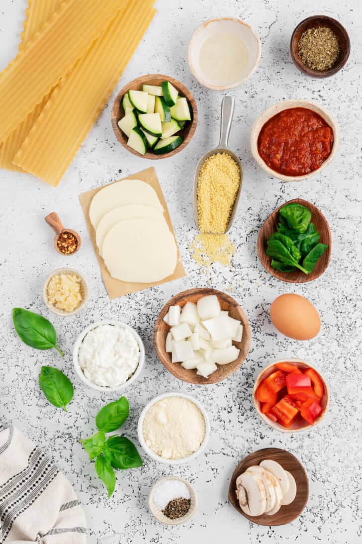 Ingredients laid out on a white stone countertop, including pasta, cheese, vegetables, egg, couscous, herbs and spices.
