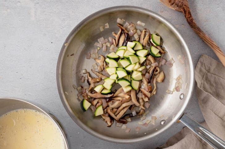 Mushrooms, shallots and zucchini being sauteed in a stainless steel skillet for a vegetarian quiche recipe.