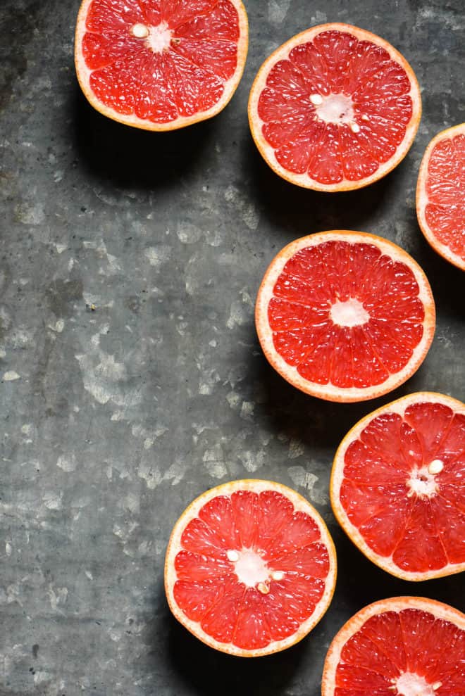 Pink citrus fruit halves on a textured metal surface.